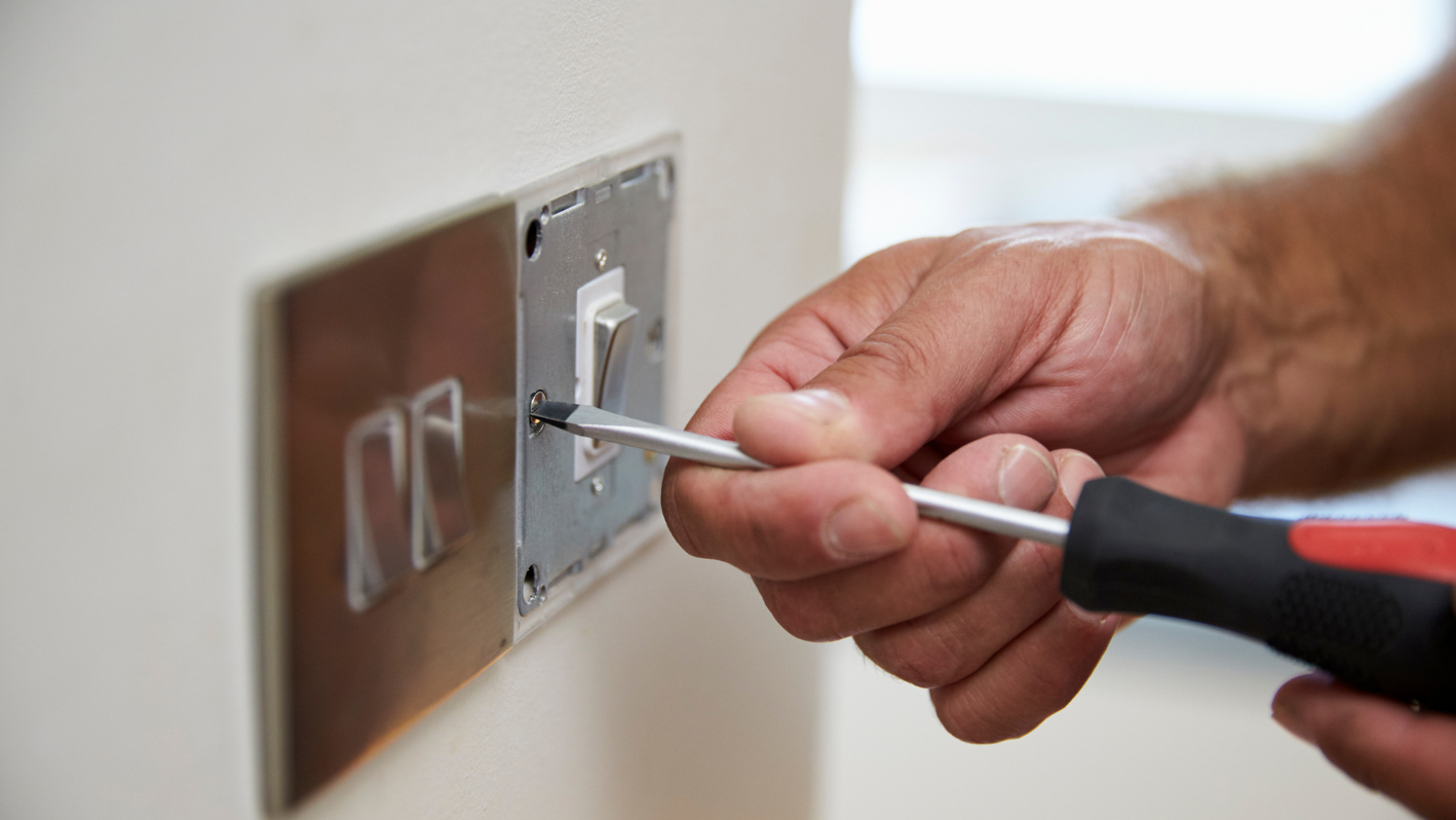 A man is fixing a light switch on a wall